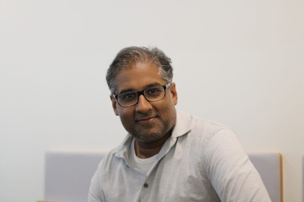 MedStack's CEO Balaji Gopalan against a white background. He is wearing a grey quarter zip sweater